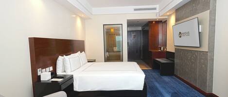 A hotel room with a large bed, a desk, a chair, a TV, and a bathroom visible through an open door.