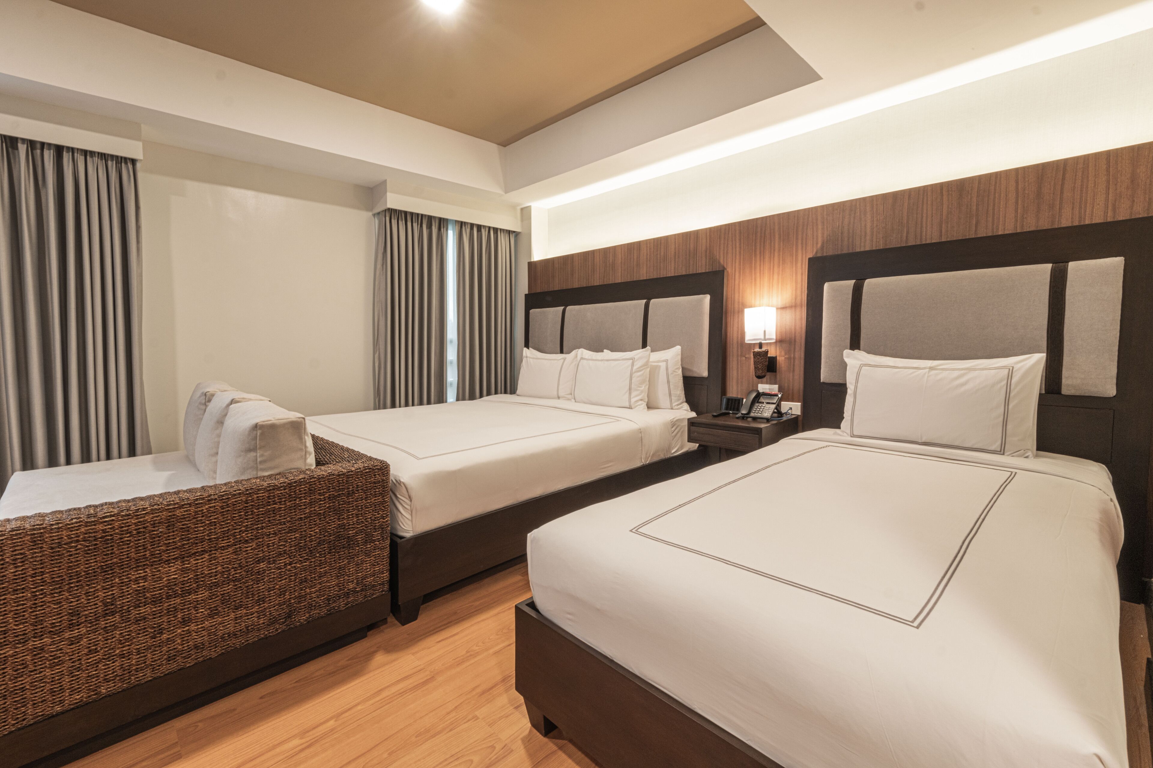 A hotel room with two beds, a sofa, a nightstand with a lamp, and a large window with curtains.