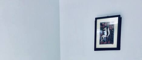 Un lit bien fait, avec une literie blanche, dans une chambre dont la tête de lit est de couleur sombre. Un tableau encadré est accroché au mur, au-dessus du lit.