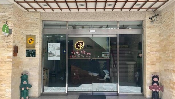 Entrada de hotel con puerta de vidrio, un letrero con caracteres chinos y una pequeña decoración de rana a la izquierda.