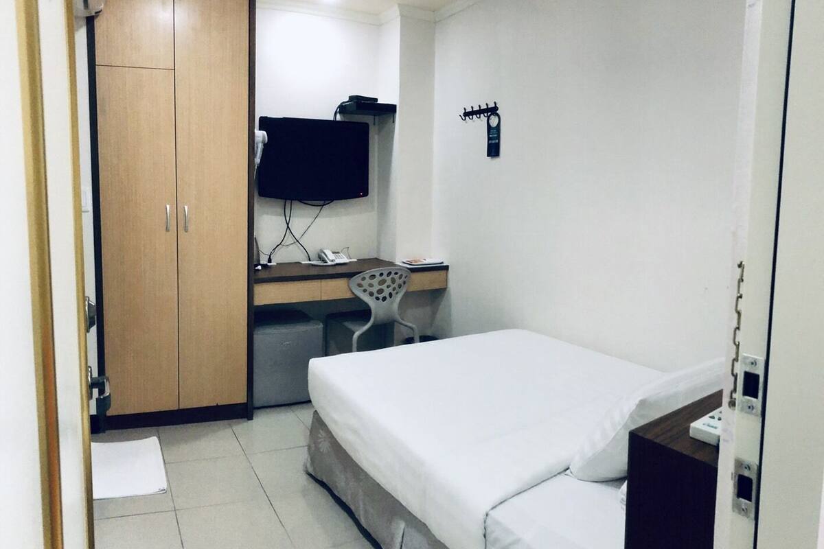 A small, clean room with a bed, a desk with a chair, a TV, and a wardrobe.