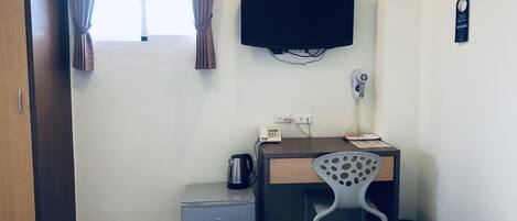 Habitación de hotel con cama, escritorio con silla, un mueble pequeño, televisor, secador de pelo y perchero.