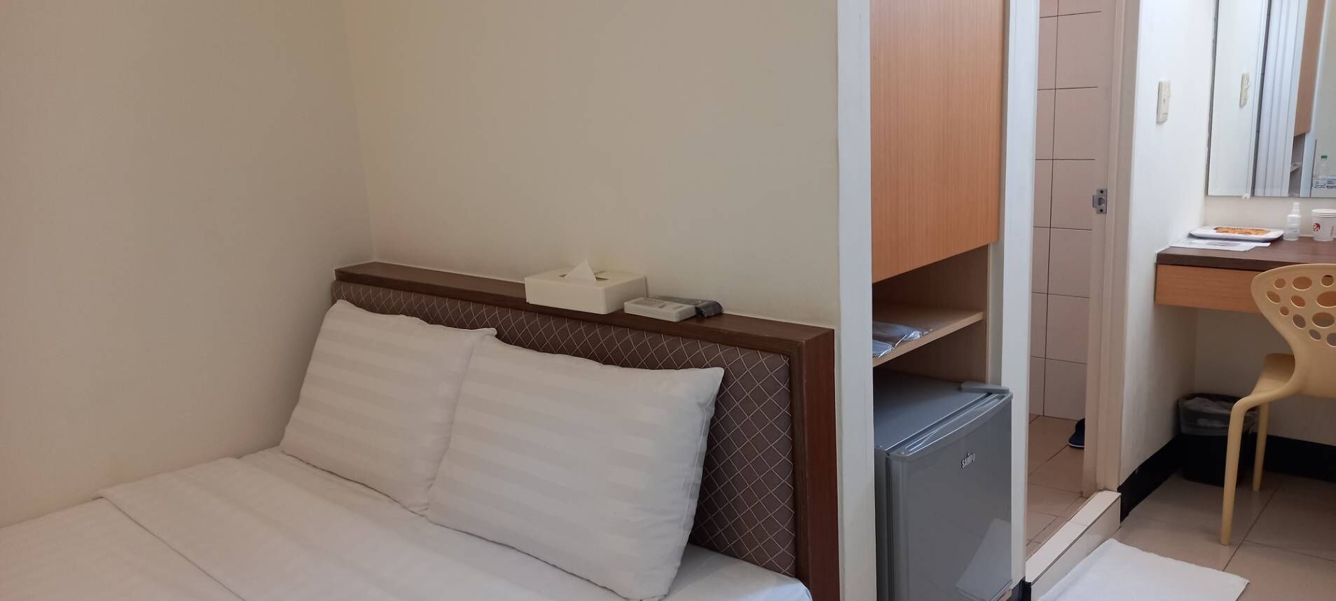 Ein Hotelzimmer mit Bett, Schreibtisch, Stuhl und kleinem Kühlschrank.