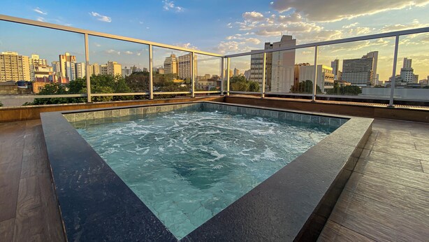A rooftop pool with a cityscape view, surrounded by glass railings and wooden decking. - Hotel Rio Vermelho (Goiania)