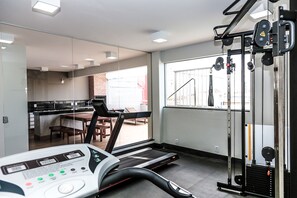 A gym with a treadmill, weight machines, and a dining area visible through the glass wall. - Hotel Rio Vermelho (Goiania)