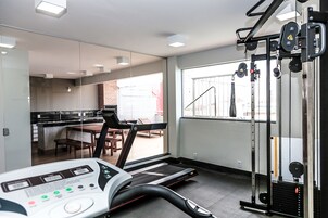 Academia com esteira, aparelhos de musculação e área de refeições visíveis através da parede de vidro.