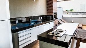 A modern kitchen with a black countertop, white cabinets, and a brick oven. - Hotel Rio Vermelho (Goiania)
