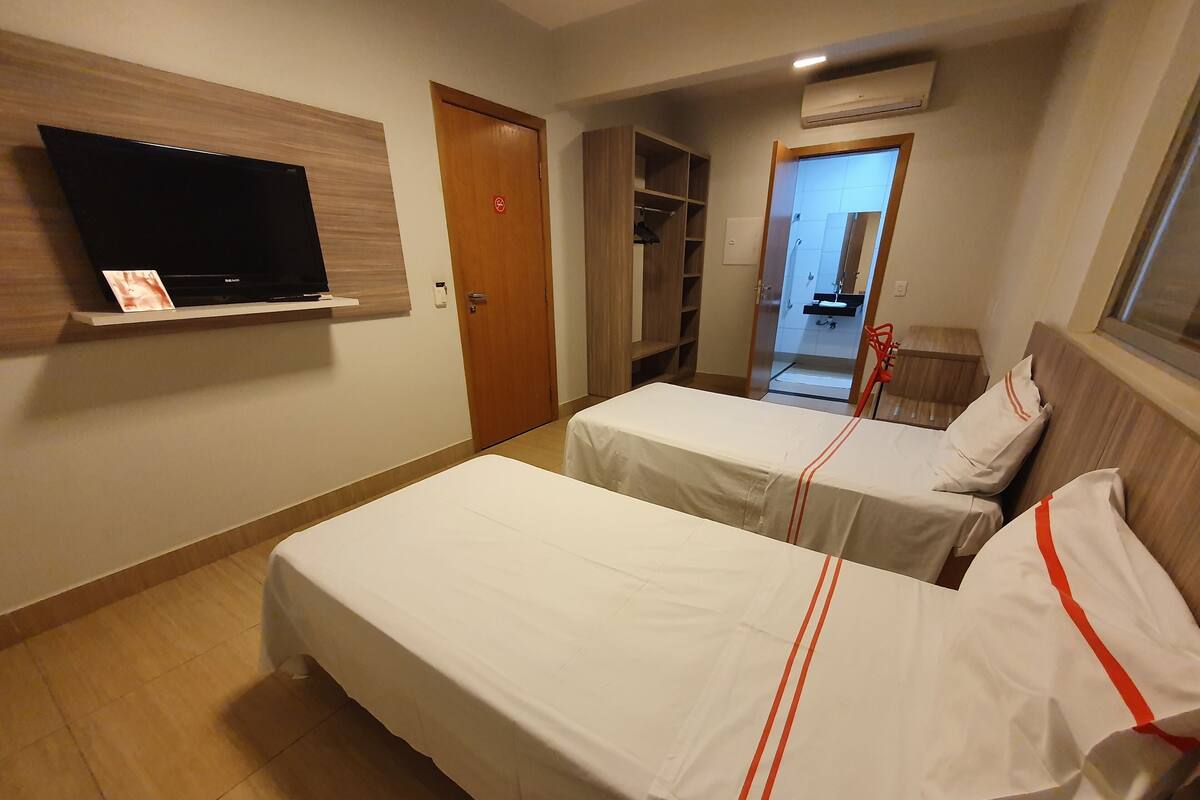 Une chambre d’hôtel avec deux lits, un téléviseur fixé au mur et une armoire.