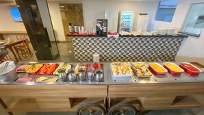 A buffet setup with various food items and condiments, a refrigerator, and a coffee machine. - Hotel Rio Vermelho (Goiania)