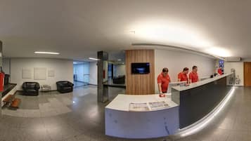 Zona de recepción con un mostrador curvo, un televisor de pantalla plana y tres empleados con uniformes rojos.