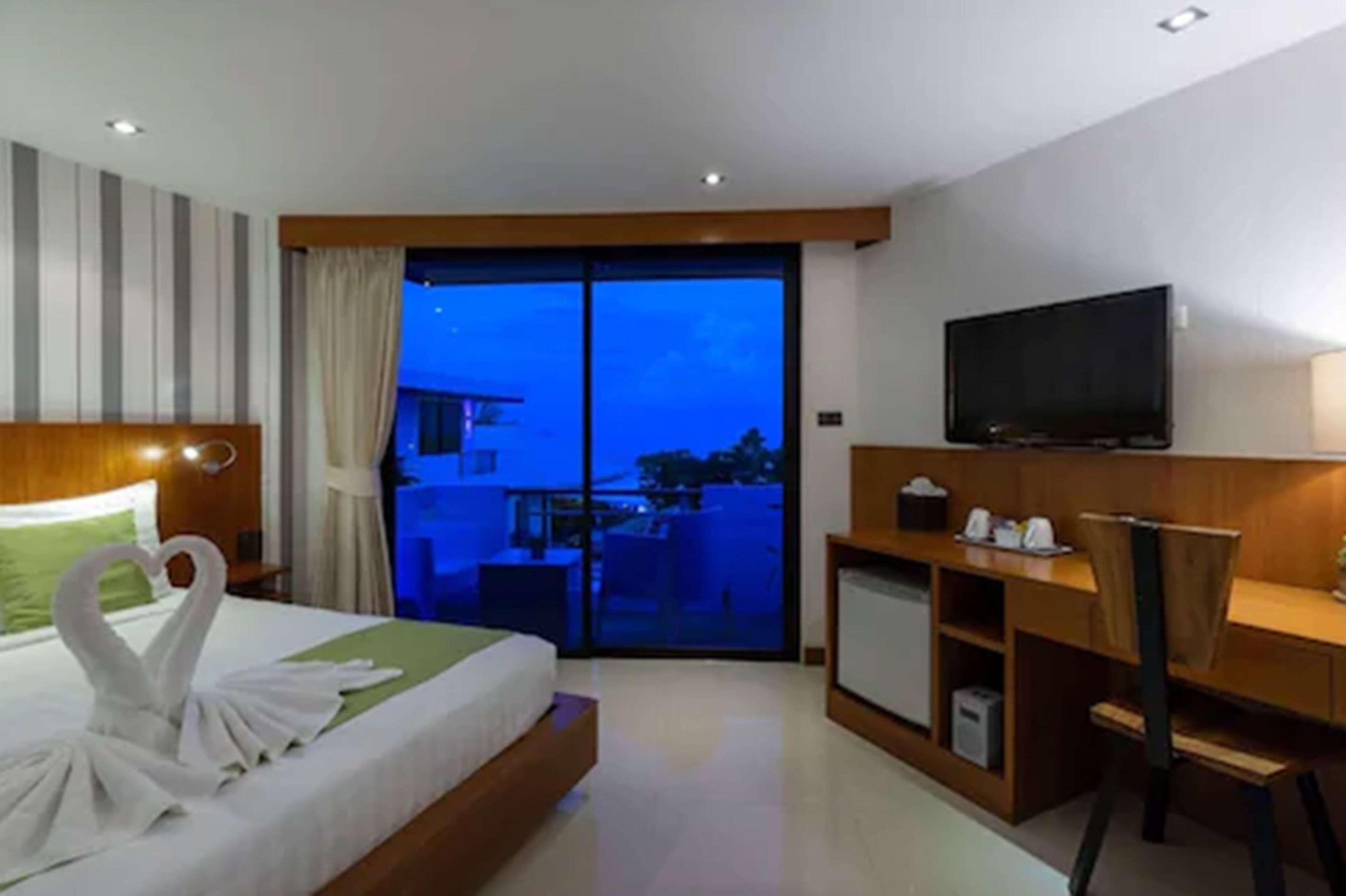 Una habitación de hotel moderna con una cama grande, un escritorio, televisión y un balcón con vistas a la ciudad.