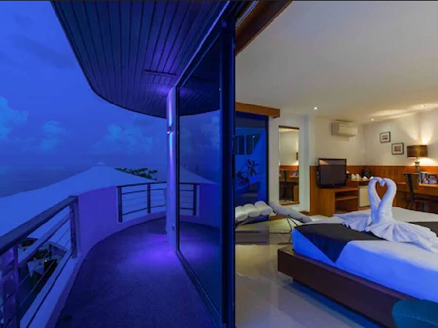 Een moderne hotelkamer met balkon, een bed met een handdoek in de vorm van een hart, een bureau en een televisie.
