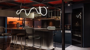 A modern bar area with a unique light fixture, bar stools, and a kitchen in the background. - OLAH Poshtel - Taichung Station (Taichung)