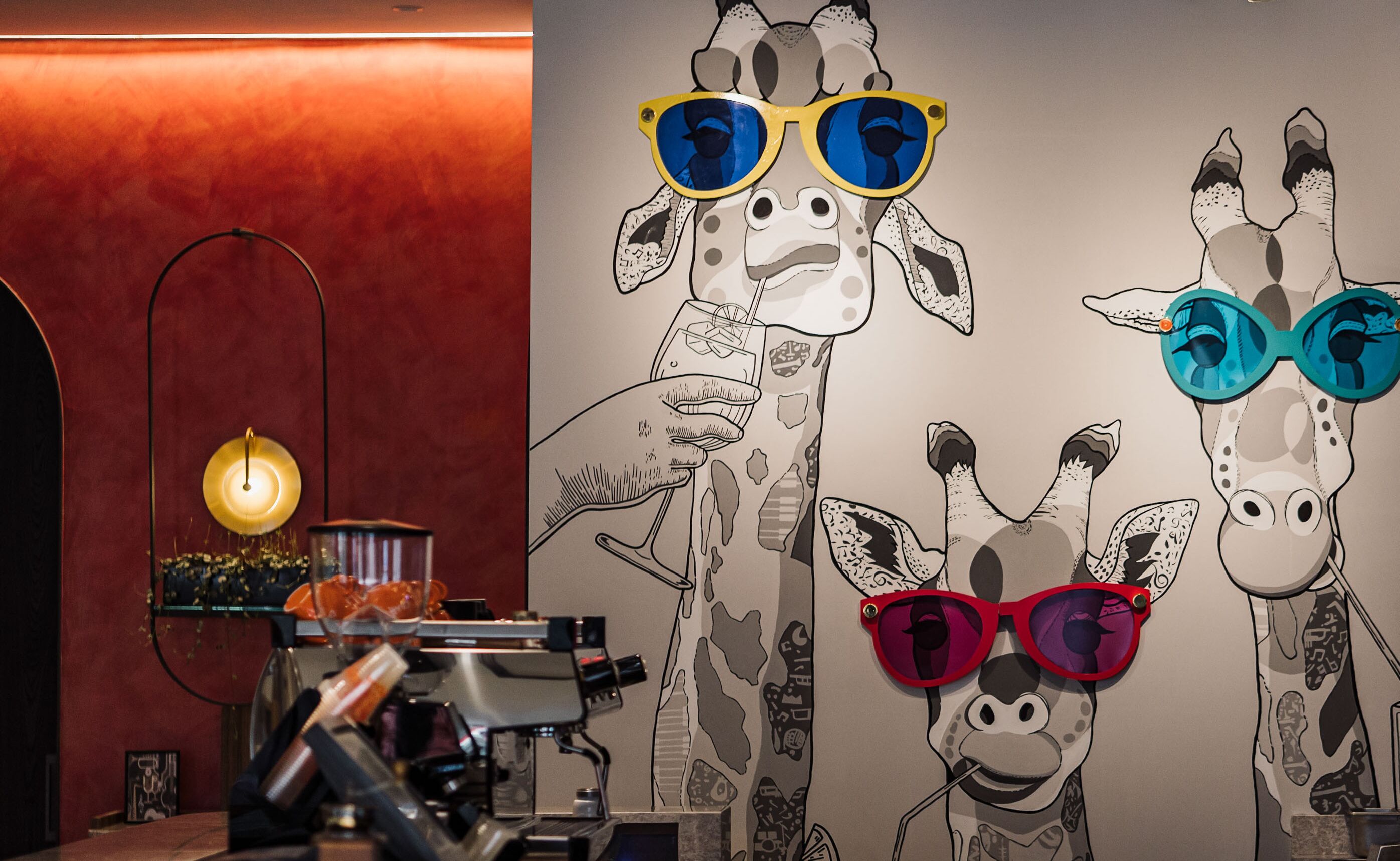 A wall with giraffe illustrations wearing sunglasses, a coffee machine, and a lamp.