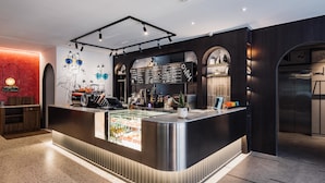 A modern bar area with a stainless steel counter, a menu board, and a seating area with a red wall and a plant. - OLAH Poshtel - Taichung Station (Taichung)