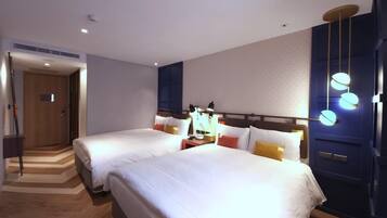 A hotel room with two beds, a nightstand, and a desk lamp.