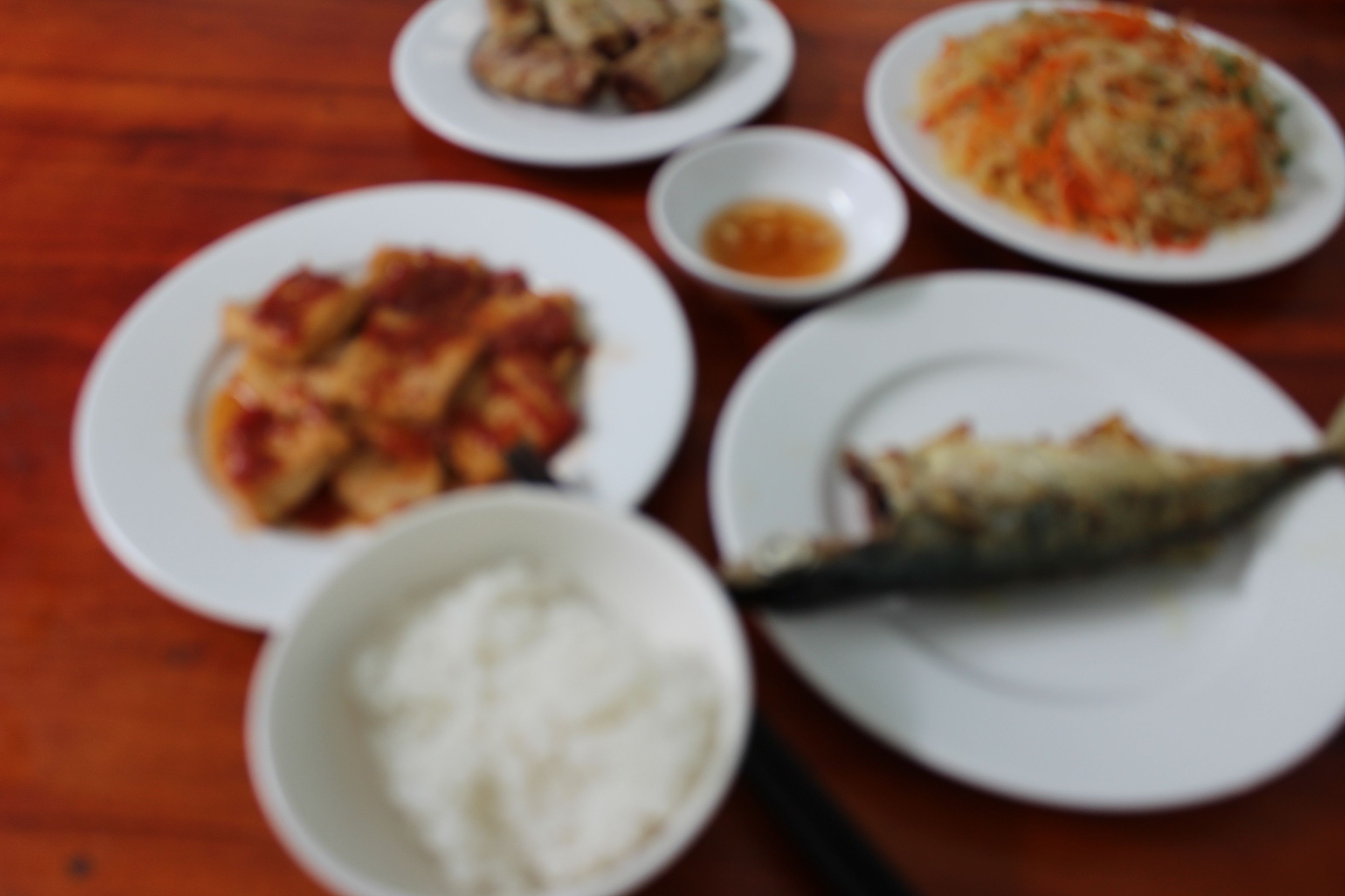 Une table où l’on trouve différents plats, notamment du poisson, du riz et des légumes.