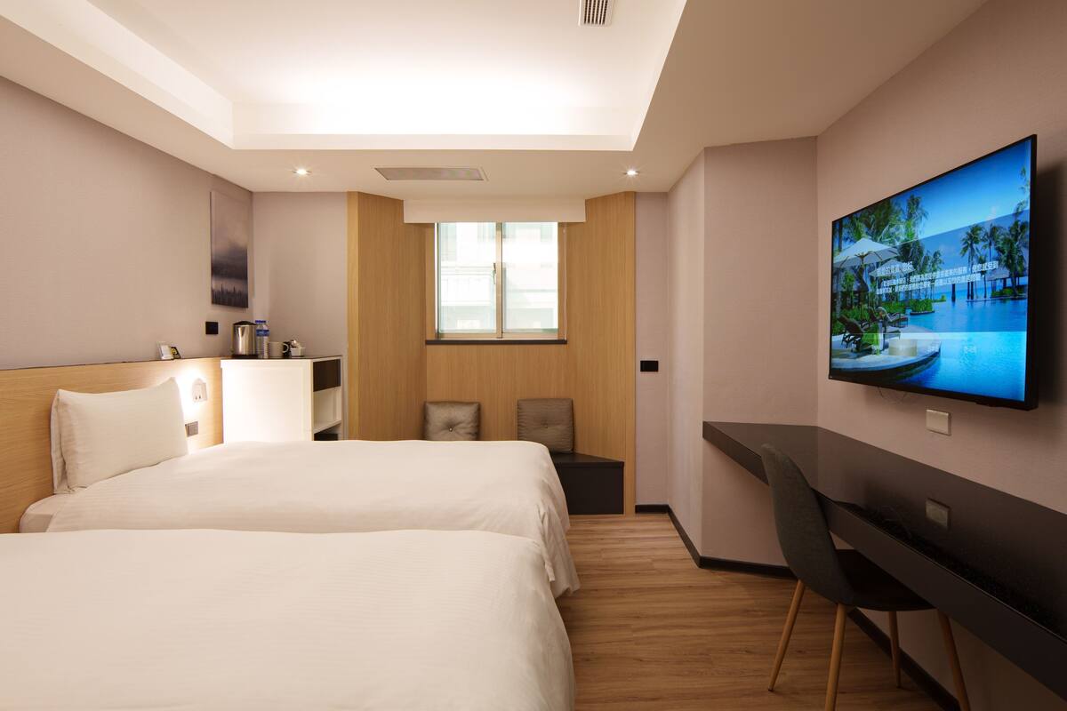 A hotel room with a bed, desk, TV, and a window.