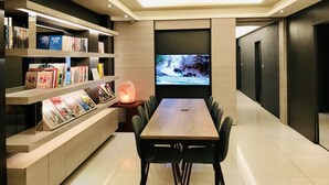A modern living room with a wooden dining table, black chairs, a bookshelf, and a television. - HUB Hotel Tucheng (New Taipei City)
