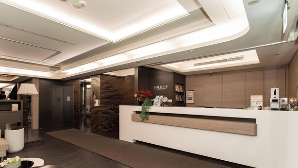 A modern hotel reception area with a reception desk, a digital screen, and a wall-mounted information board. - HUB Hotel Tucheng (New Taipei City)