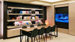 A modern library with a wooden table and chairs, bookshelves, and a large flat-screen TV. - HUB Hotel Tucheng (New Taipei City)