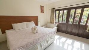 A spacious bedroom with a large bed, a wooden headboard, a nightstand, a chair, and a view of greenery through a window with curtains. - Buathong Place (Koh Samui)