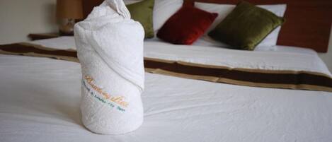 Una cama bien hecha con una toalla blanca enrollada en el centro, un cabecero marrón y varios cojines en rojo, verde y blanco.