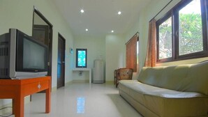 A living room with a sofa, a television on a wooden table, a window with curtains, and a refrigerator in the background. - Buathong Place (Koh Samui)
