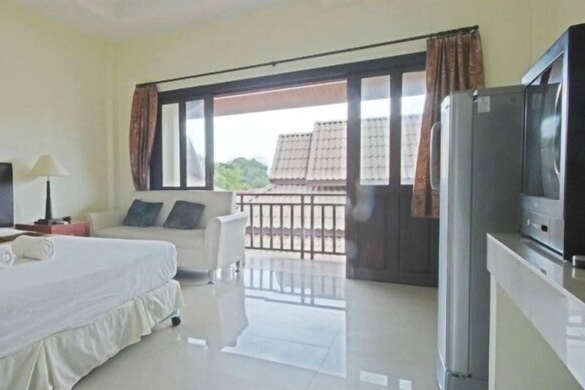 A hotel room with a large bed, a TV, a balcony with a view, and a refrigerator.