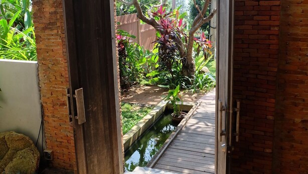 Entrada de tijolos para uma área de jardim com um pequeno espelho d'água e pedriscos.