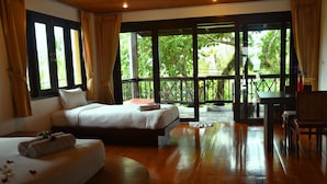 Quarto de hotel com duas camas, uma mesa de jantar e vista para vegetação exuberante através de amplas janelas.