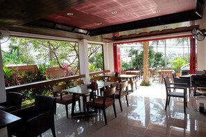 An indoor dining area with tables and chairs, large windows offering a view of greenery outside. - Samui Jean Resort (Koh Samui)