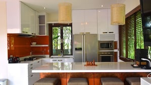 Cozinha moderna com ilha central, eletrodomésticos de aço inoxidável e uma grande janela com folhagem verde.
