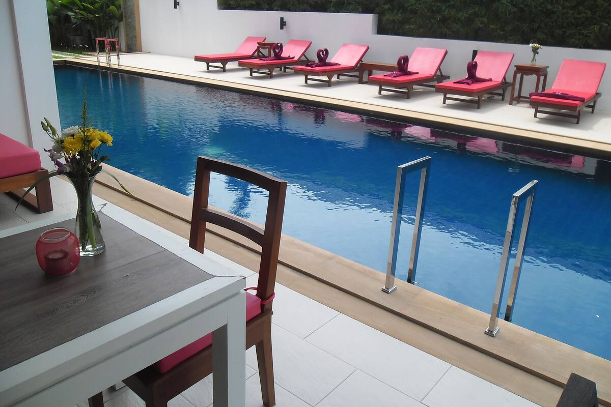 A poolside area with lounge chairs, a table with a vase of flowers, and a chair.