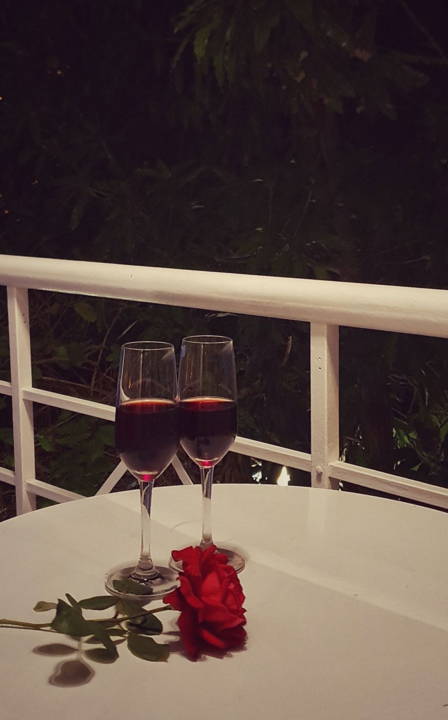 Ein Tisch mit zwei Weingläsern und einer roten Rose.