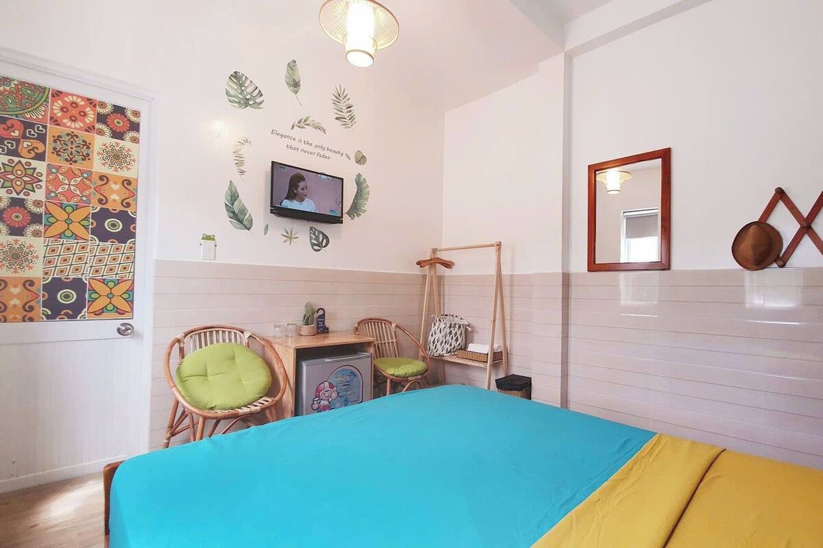 A bedroom with a bed, two chairs, a small table, a TV, and decorative wall elements.