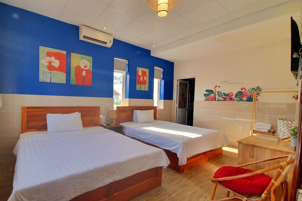 A hotel room with two beds, a wooden floor, and a red chair.