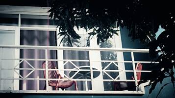A balcony with a metal railing, two chairs, and a window with reflections of trees.