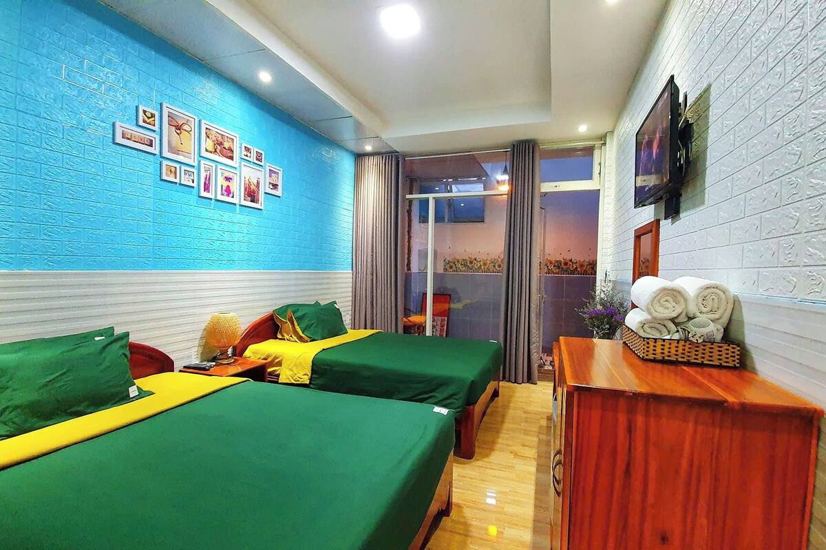 A hotel room with two beds, a wooden dresser, a TV, and a blue wall with framed pictures.