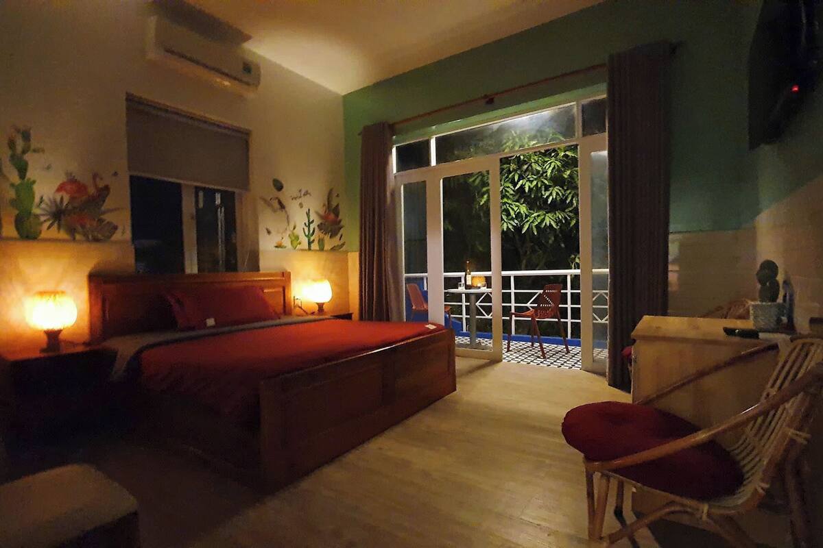 A bedroom with a bed, bedside lamps, a chair, and a view of the outside through a glass door.
