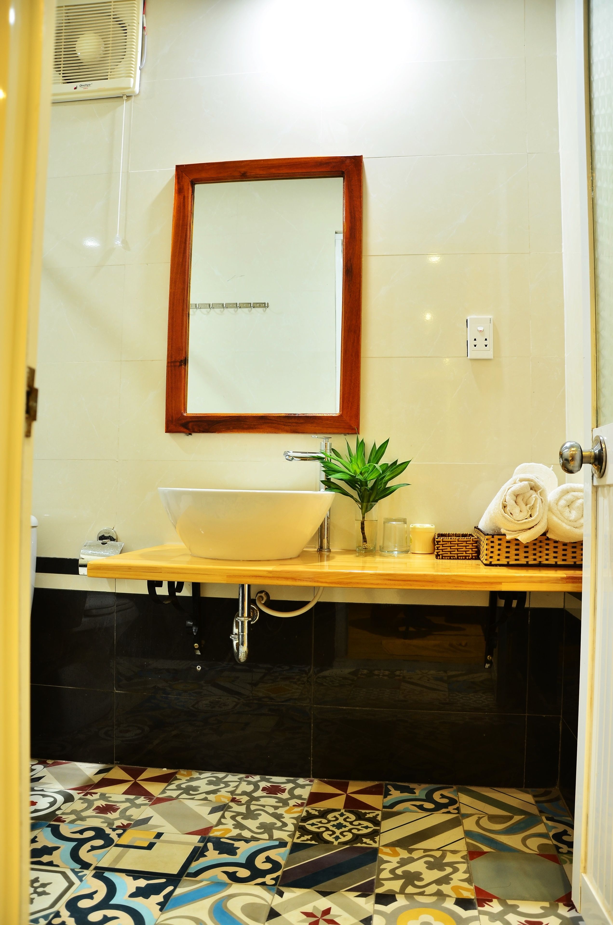 Un baño con un lavamanos blanco, un espejo con marco de madera, una planta en maceta y toallas sobre la encimera.
