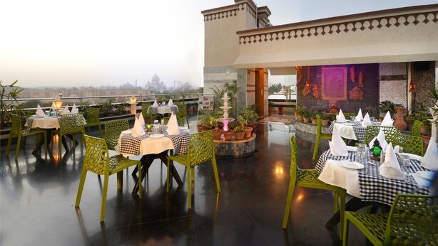 Un restaurante en la azotea con mesas dispuestas para comer, rodeado de plantas en macetas y una vista de un edificio histórico al fondo.