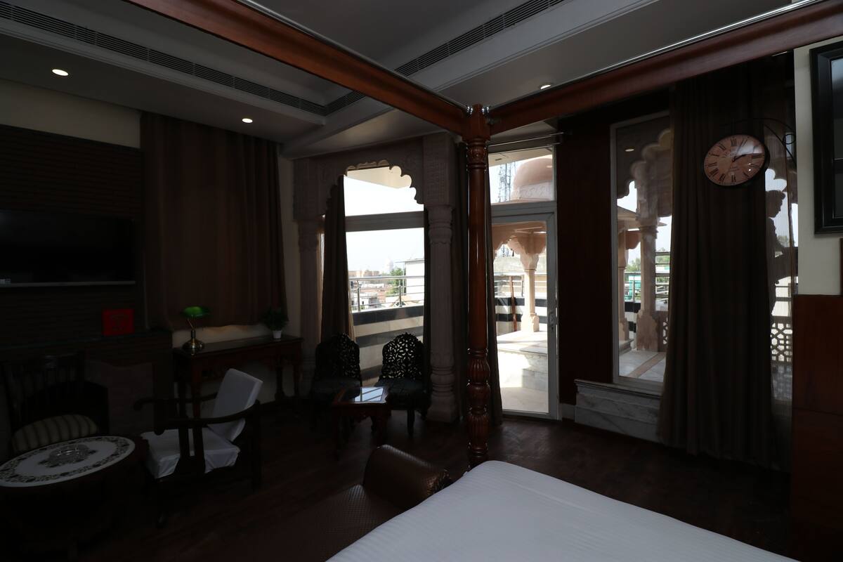 Habitación de hotel con una cama grande, televisión, zona de estar con sillas, una mesita y vistas al exterior a través de una puerta.