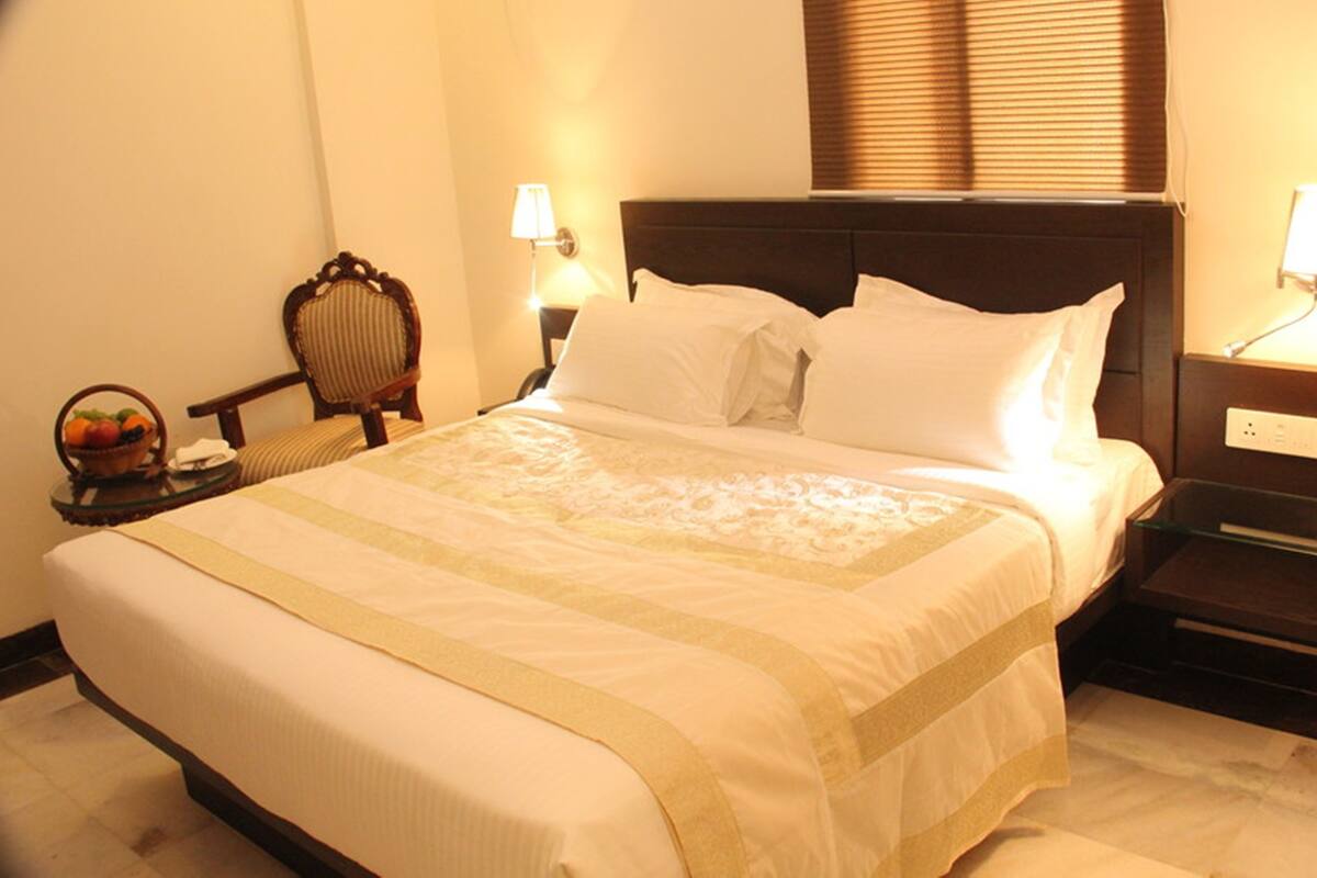 Una cama bien hecha con sábanas blancas y un borde decorativo, flanqueada por dos mesitas de noche con lámparas, una de ellas con una cesta de fruta.