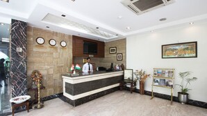 Zona de recepción de un hotel con un mostrador de mármol, un reloj, un cuadro enmarcado y una planta en maceta.