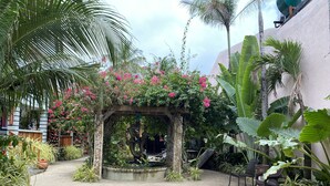 Un jardín con un arco de piedra, diversas plantas y una zona de estar.