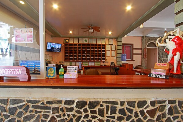 A reception area with a wooden counter, a reception desk, a wall-mounted television, and a ceiling fan.