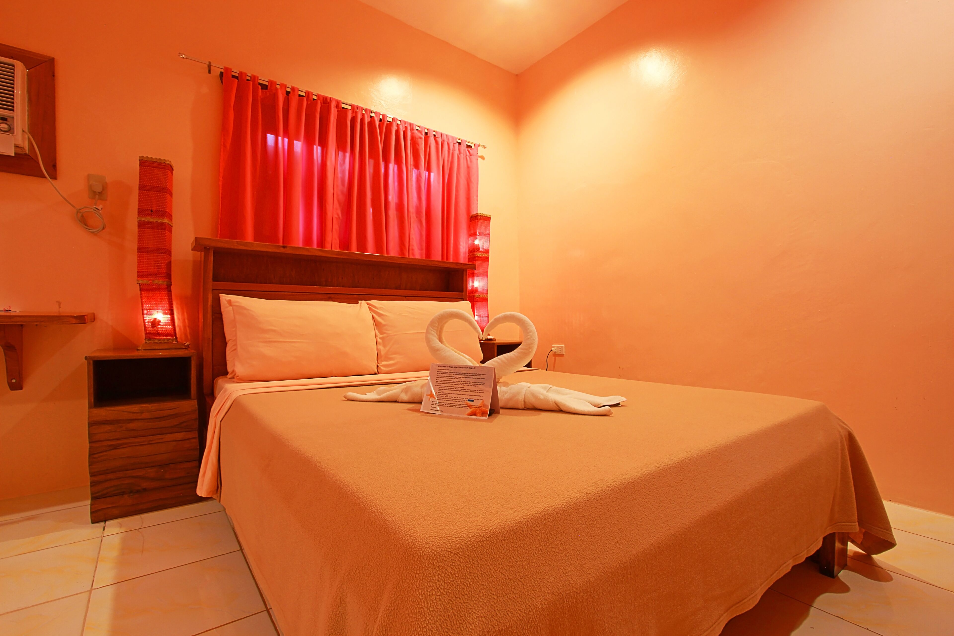 A hotel room with a large bed, a nightstand, a red curtain, and a wall-mounted heater.