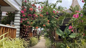 Un sendero bordeado de plantas y flores tropicales, que lleva a un edificio con techo de paja.
