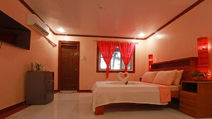 Habitación de hotel con cama, televisor montado en la pared, refrigerador y ventana con cortinas rojas.